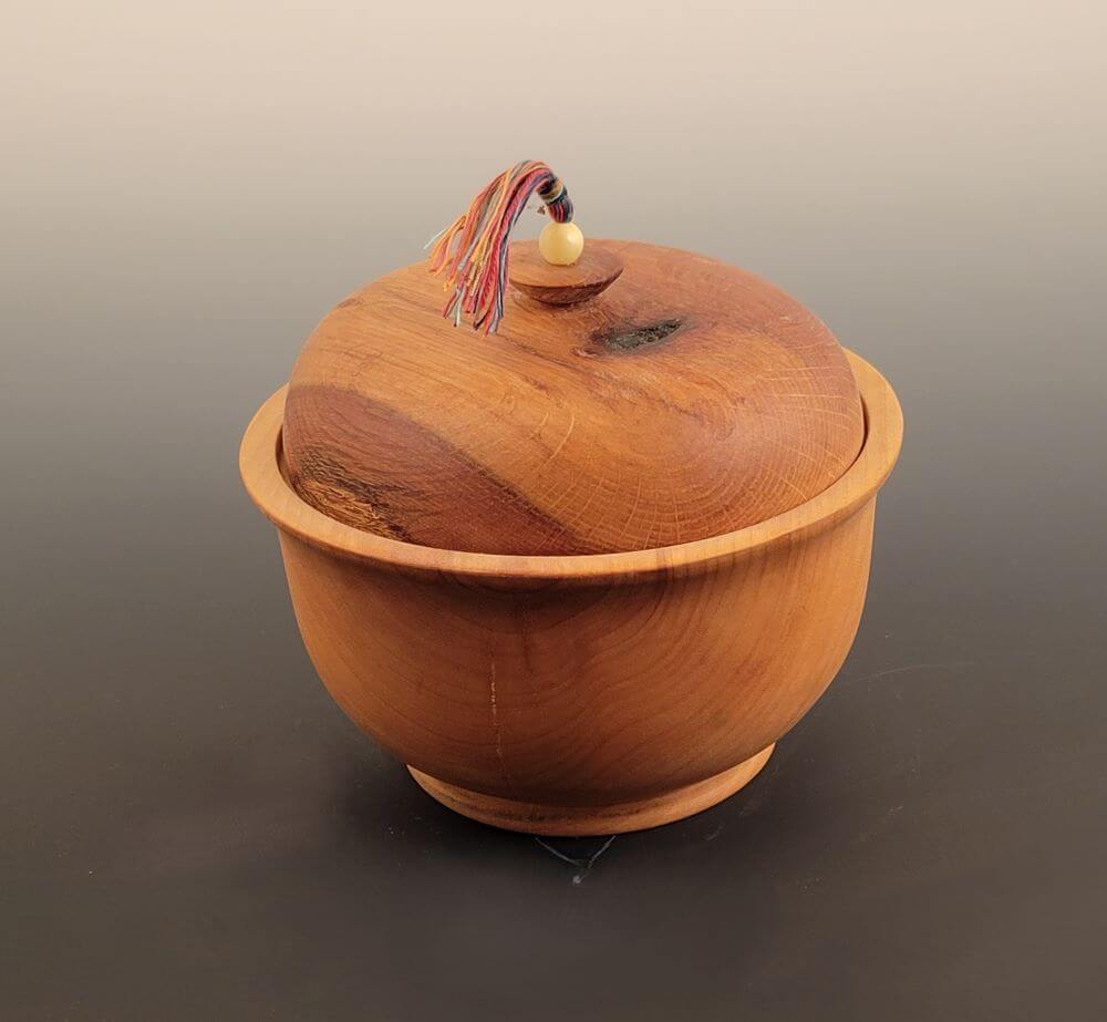 Lidded bowl with tassel & stone bead. Natural flaw. Maple with oak top.